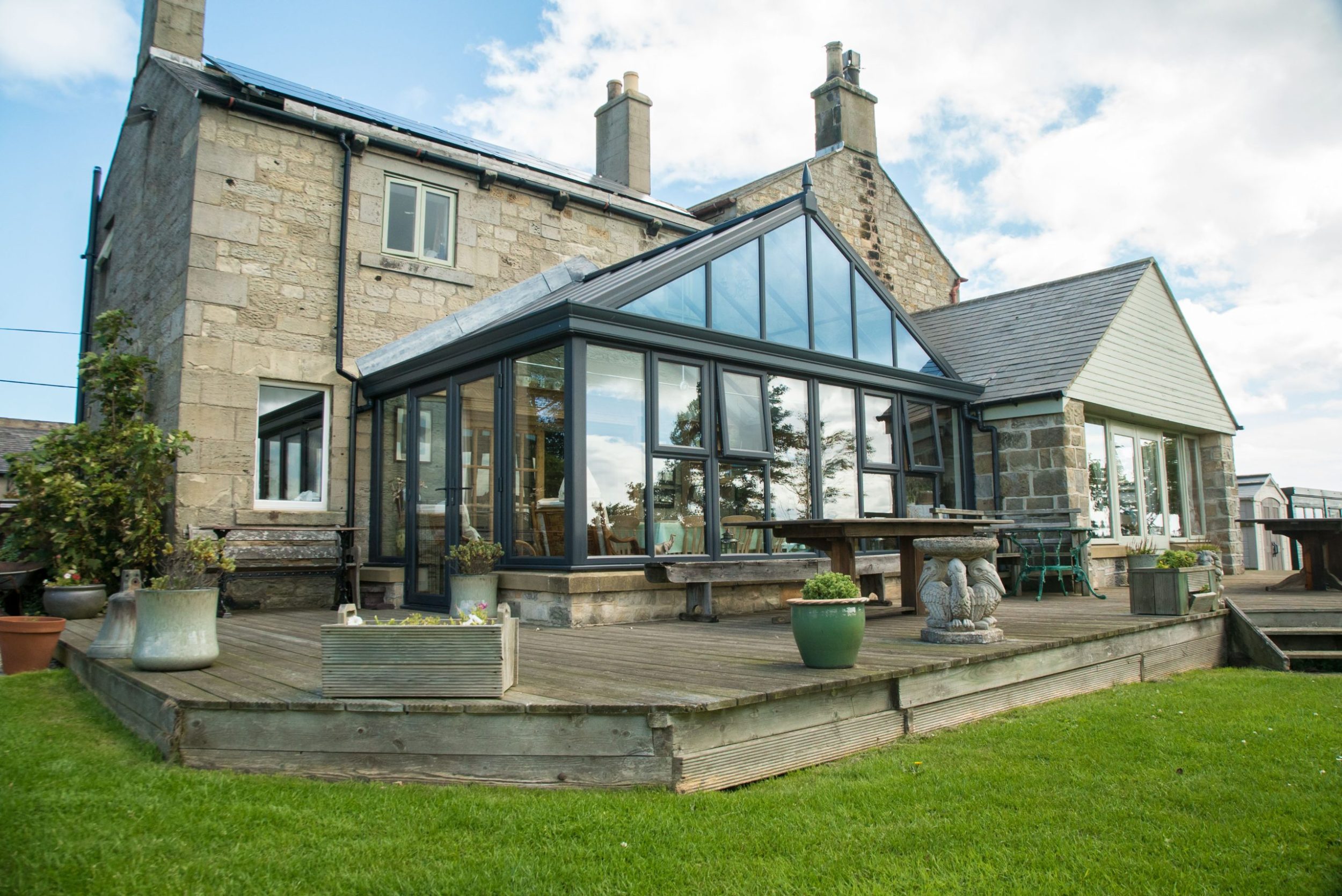 Charcoal grey fully glazed conservatory on the back of a large house with a deck leading to the back garden.