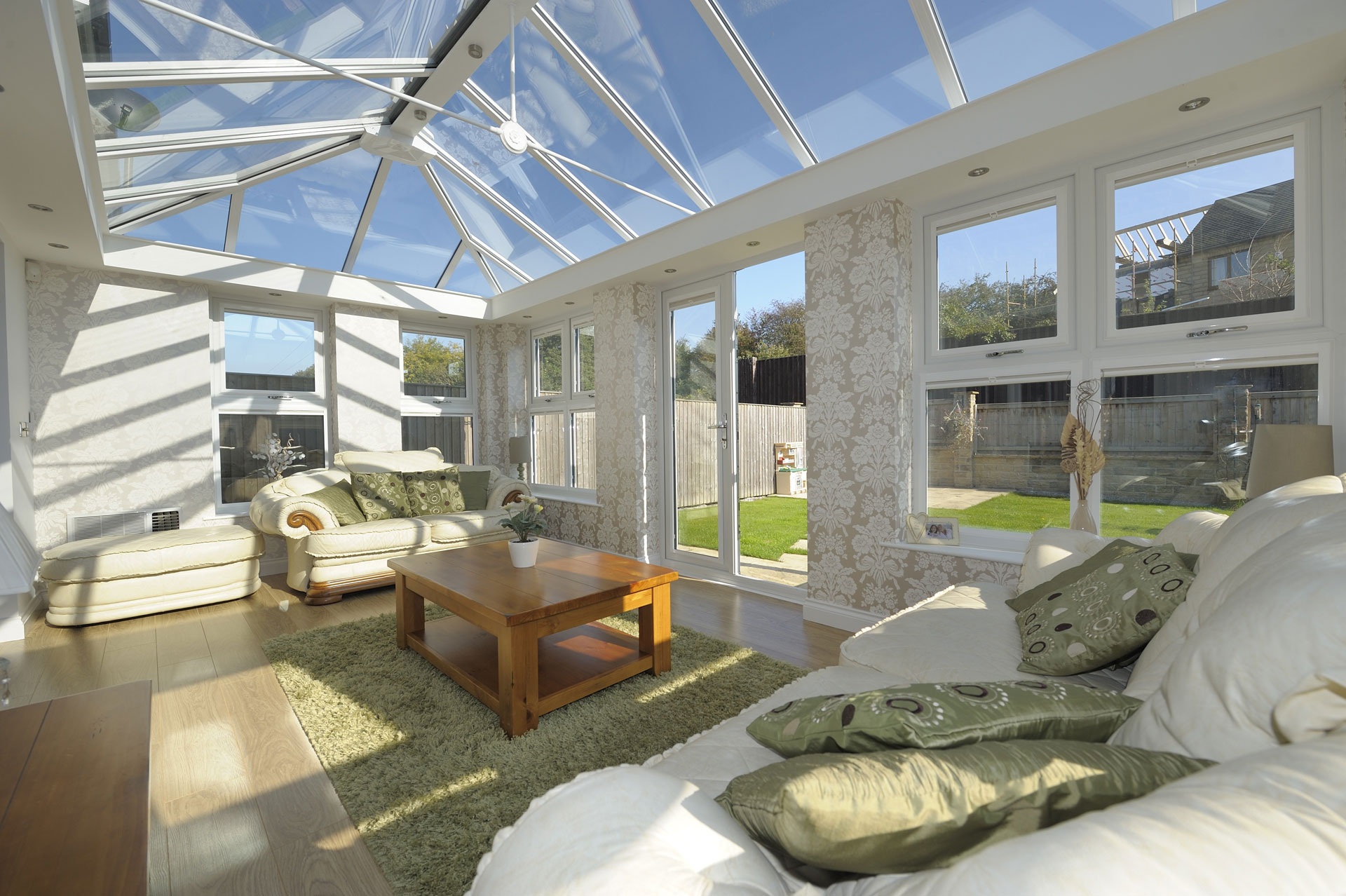 Conservatory with a glass roof and a garden view with sofas in.