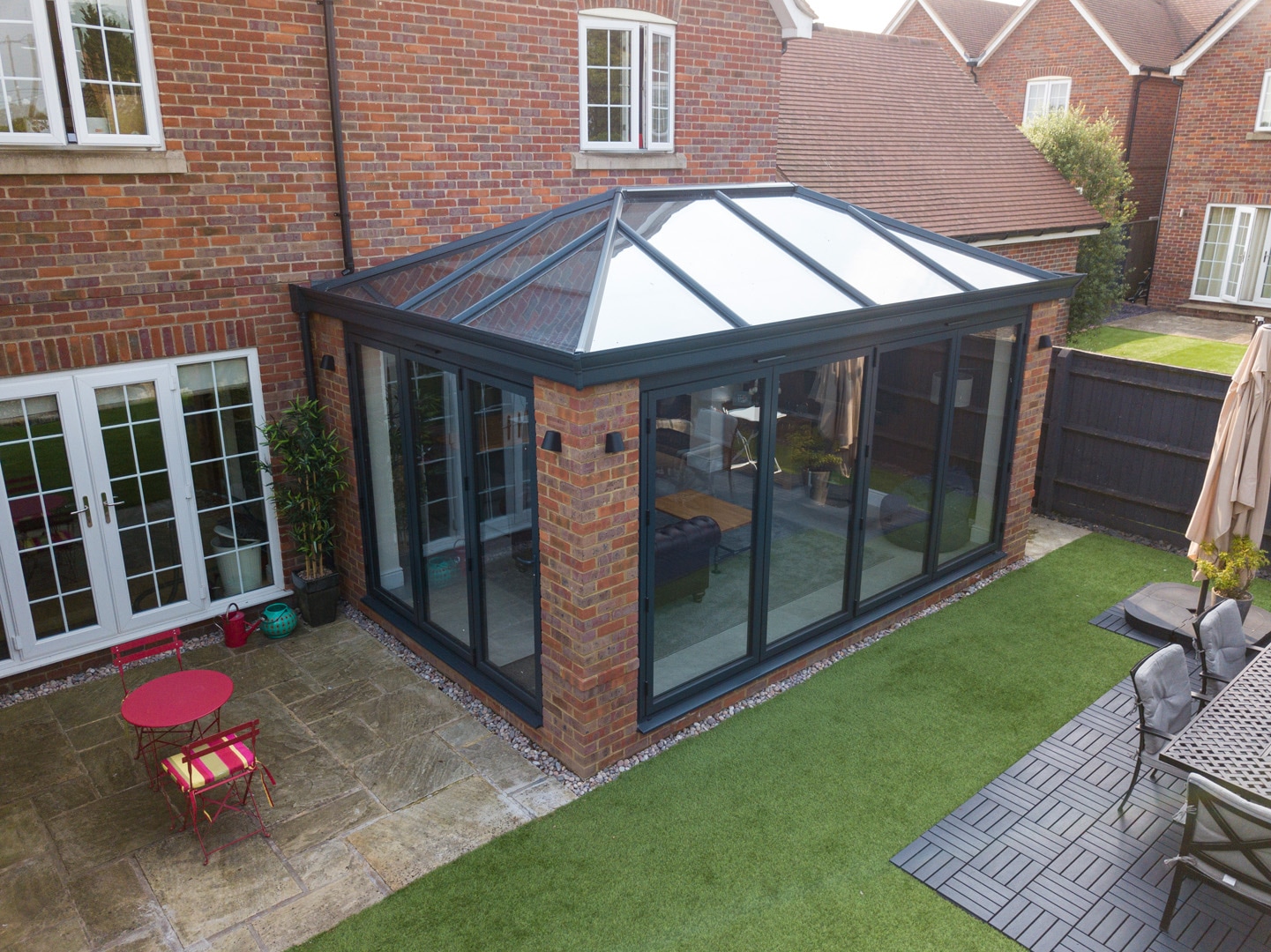 A Bespoke modern hybrid orangery-conservatory with a black frame and brick columns.