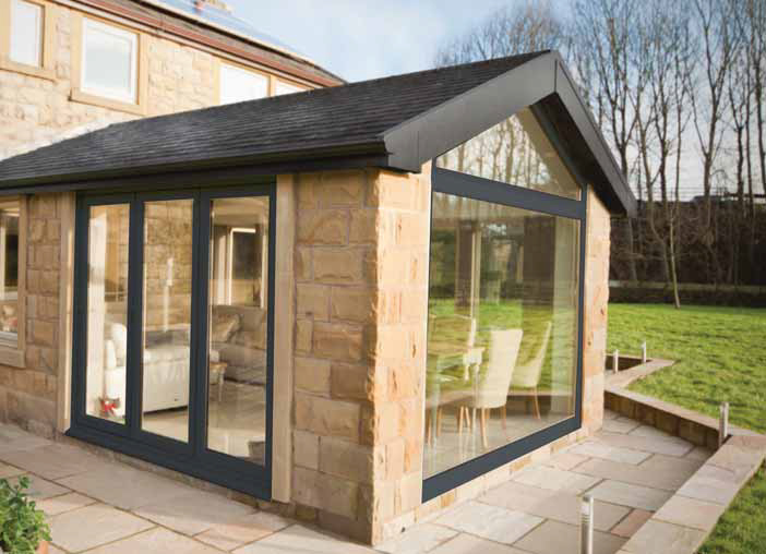 Gable end conservatory with large stone bricks and dark colour window frames.