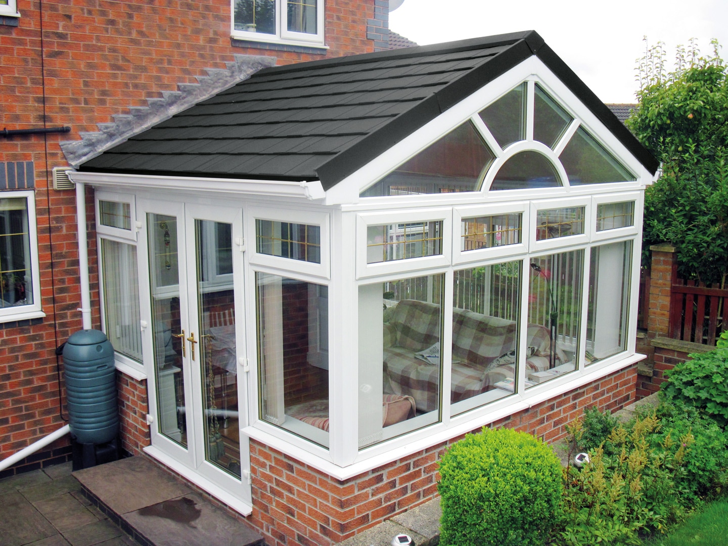 Modern tiled conservatory roof by Enhance Conservatories with a skylight, providing a seamless integration with the existing brick house, offering a blend of traditional aesthetics and contemporary design to enhance natural light and indoor comfort