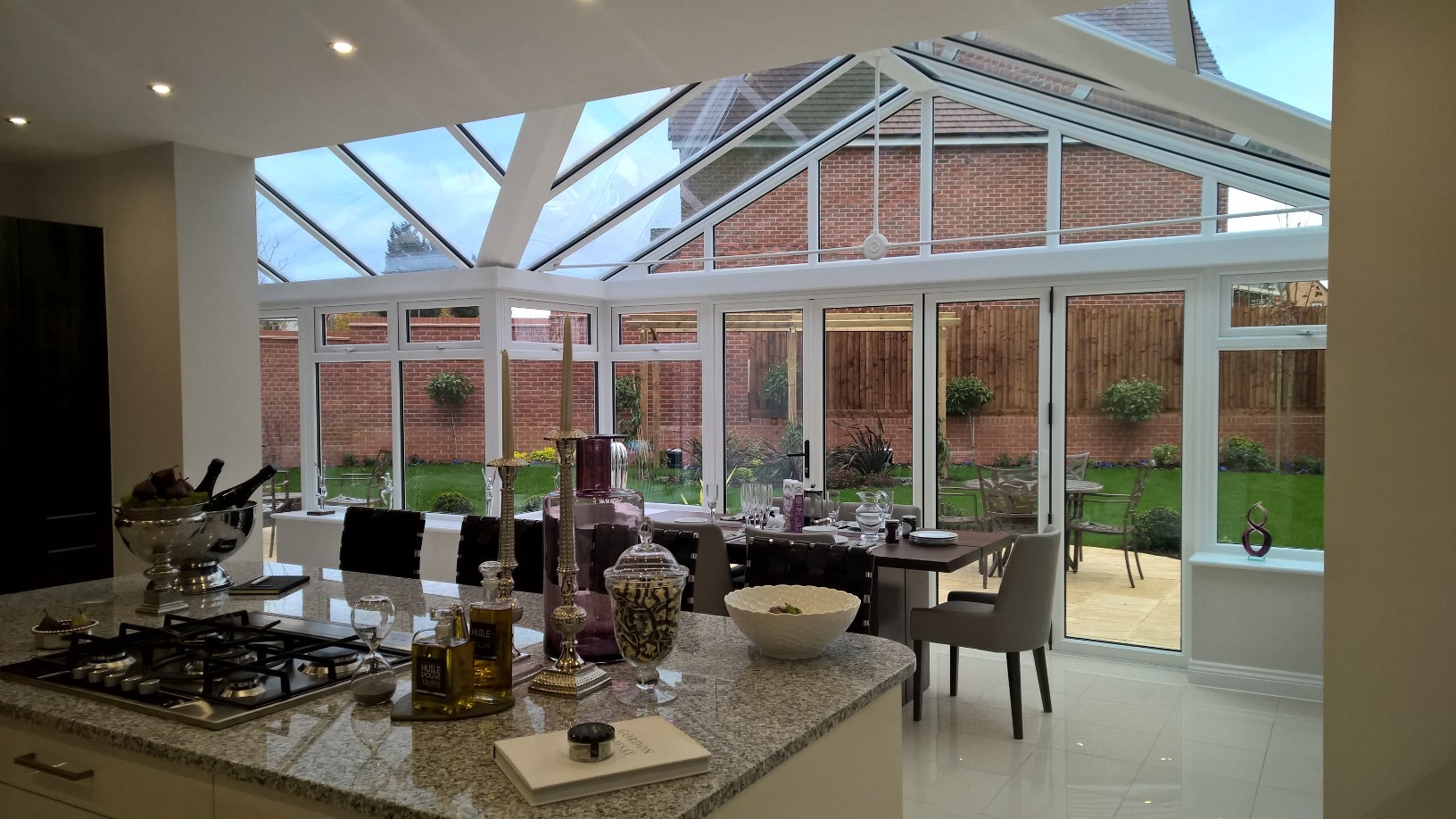 A bespoke uPVC conservatory style housing a kitchen and dining space, with glass roof and glazing looking out into the garden.