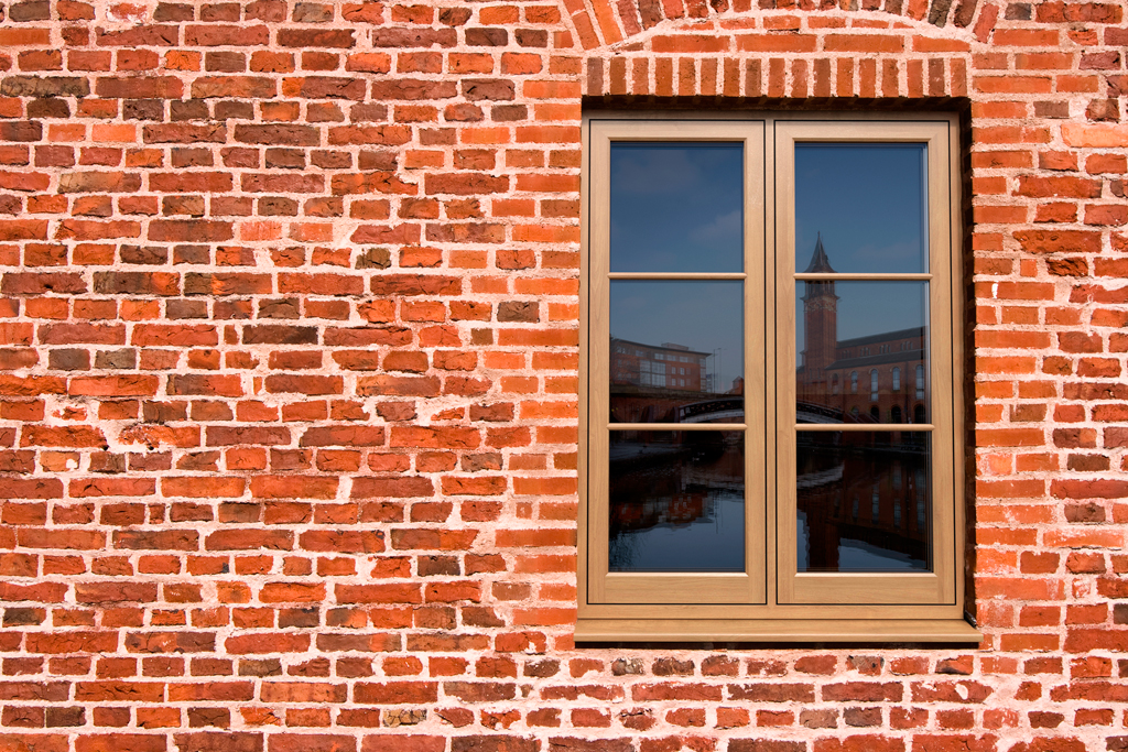 Close-up view of a deep mahogany-stained uPVC casement window with a reflective glass pane, set in a light-colored stone wall. The reflection shows a silhouette of a dog and hints of the room's interior, while the window itself boasts a polished, wood-grain finish that complements the rustic aesthetic of the building
