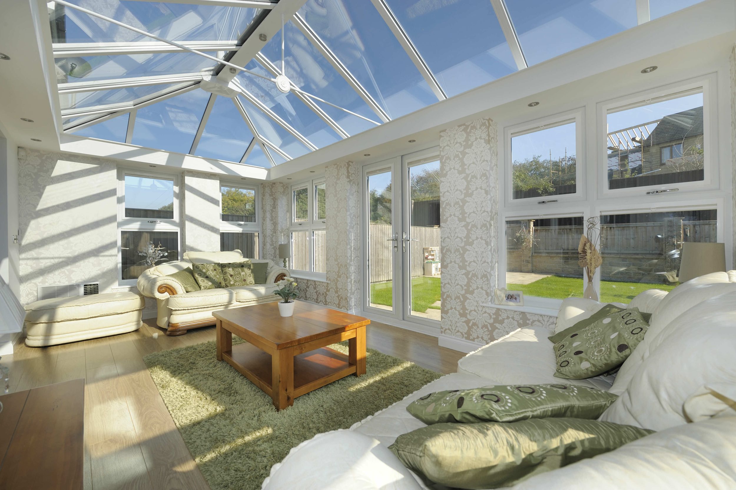 Glass roofed conservatory with sofas and wooden table in the centre