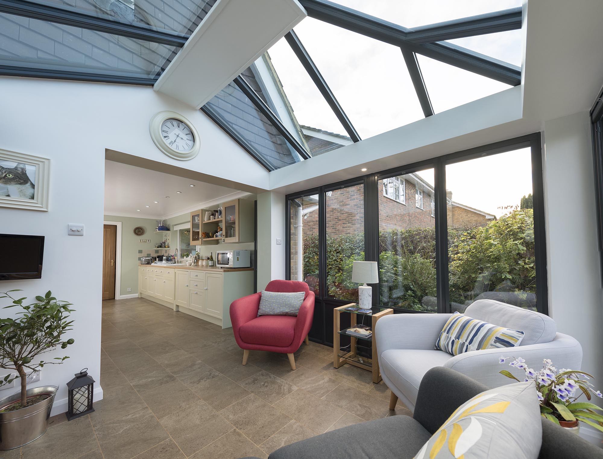 An elegant glass-to-floor conservatory with extensive transparent panels reaching down to the ground, providing an uninterrupted view of the garden and maximizing natural light, creating a bright and immersive indoor-outdoor experience