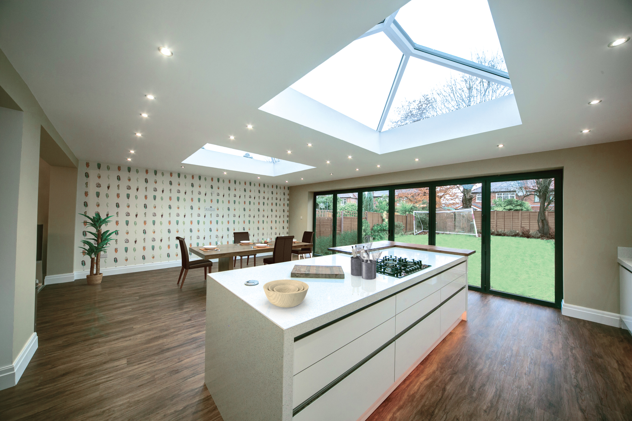 Sleek and spacious kitchen extension with contemporary design, showcasing a large central island, modern appliances, and an abundance of natural light from overhead skylights and wide glass doors leading to the garden