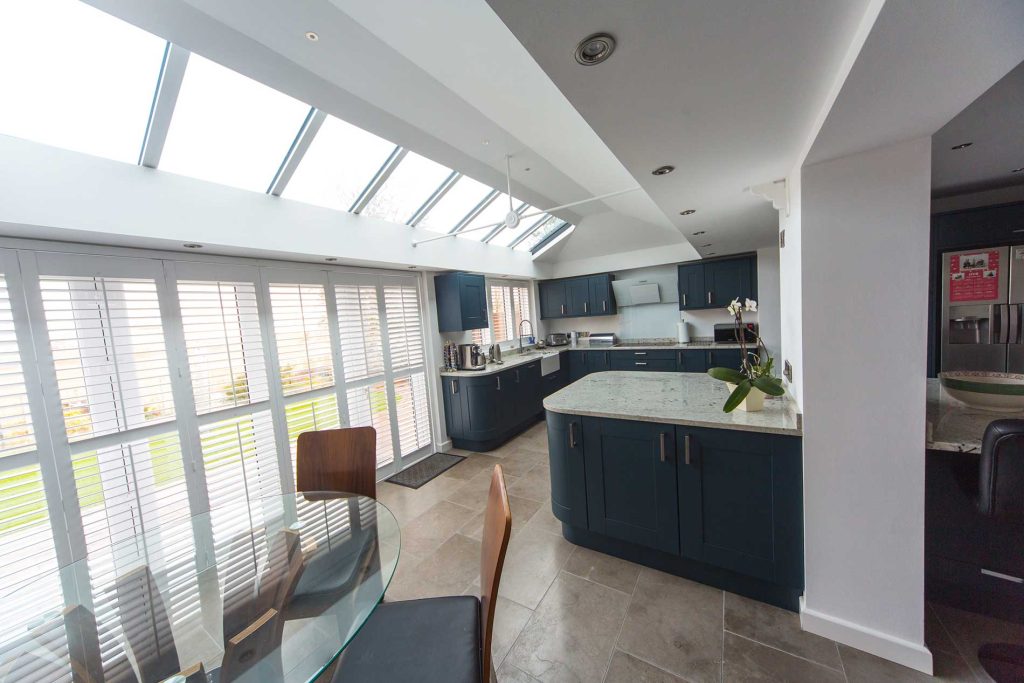 Modern kitchen extension featuring large glass windows and doors, providing a bright and airy space. The design elegantly blends the kitchen with the outdoors, creating a seamless transition and enhancing the home's overall aesthetic.