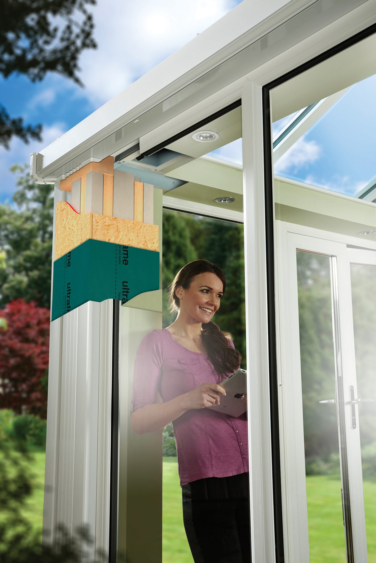A smiling woman in a purple top stands inside a conservatory with modern white frames, holding a tablet. A cross-section of the conservatory wall reveals layers of insulation and construction materials, highlighting the energy-efficient design