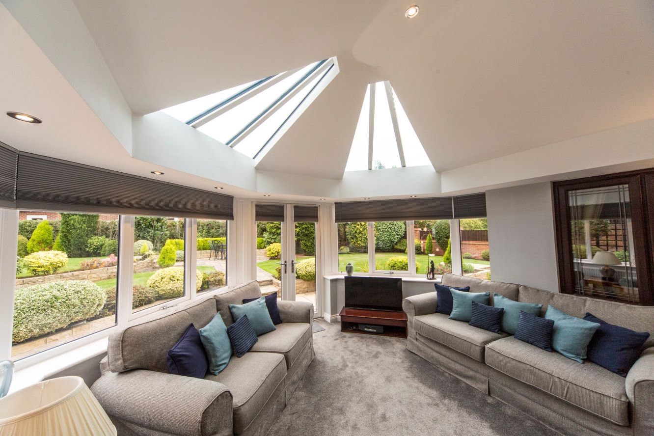 inside view of conservatory with two sofas and white upvc french doors looking out to an expansive garden