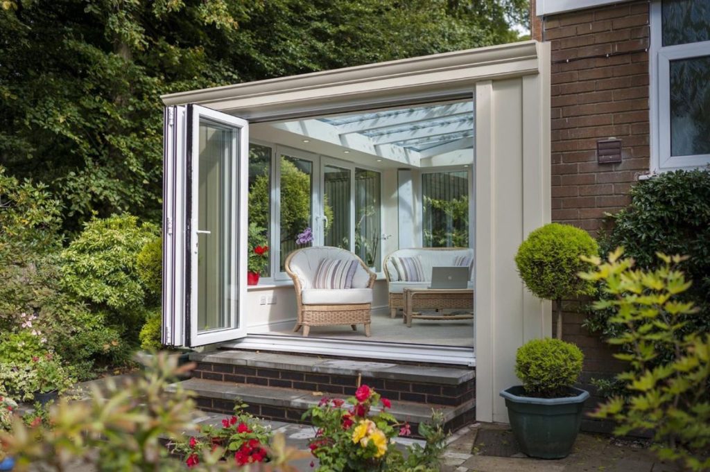 Stylish conservatory with white uPVC bi-fold doors opening to a lush garden patio, featuring wicker furniture and natural light