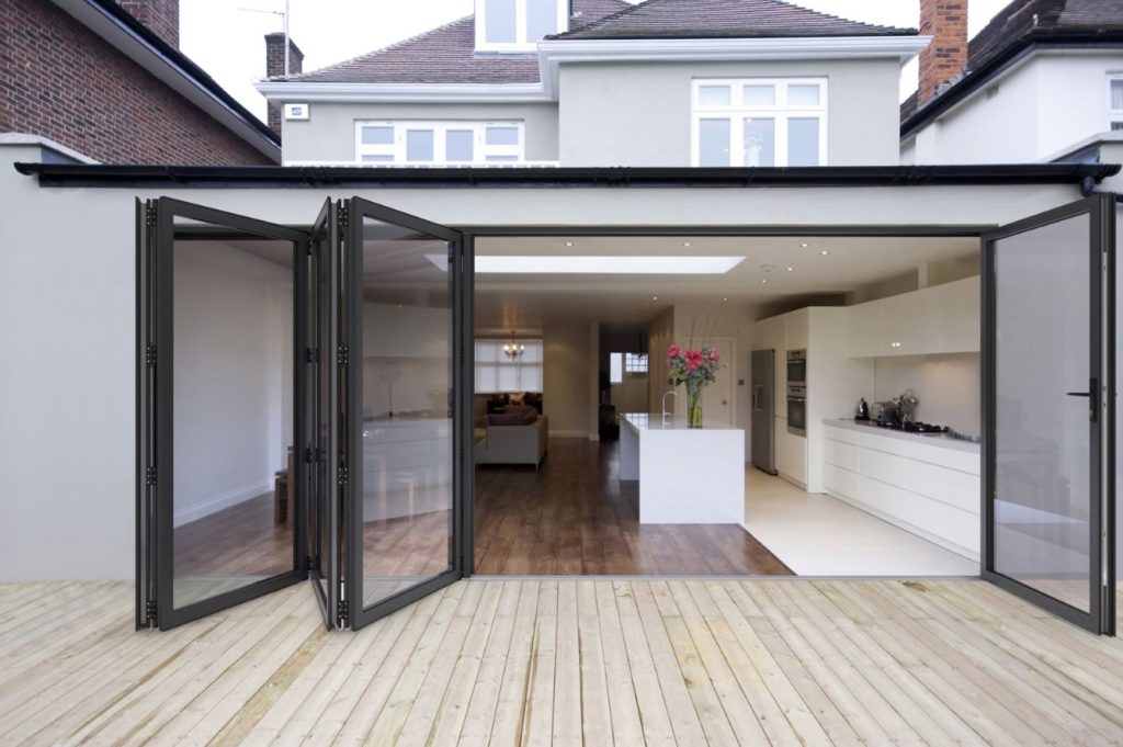 Stylish modern home extension featuring open bi-fold doors connecting a spacious kitchen and living area to an outdoor wooden deck, perfect for indoor-outdoor living