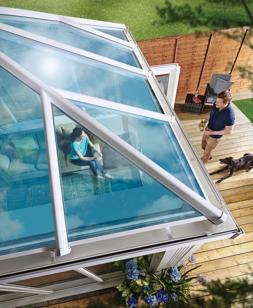 aerial view of glass roof upvc conservatory with woman sat down inside with man walking towards her with a dog