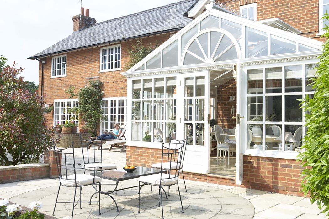A gable-end conservatory by Enhance Conservatories featuring a classic pitched roof design, with expansive glass panels allowing for ample natural light, set against a home with visible brickwork and surrounded by a well-maintained garden